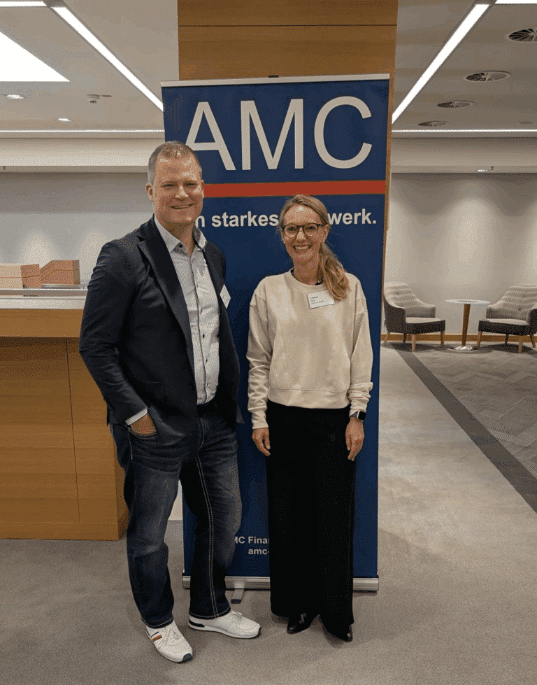 Marco Leven und Celine Spitz are standing in front of the AMC display at the AMC Meeting 2025.