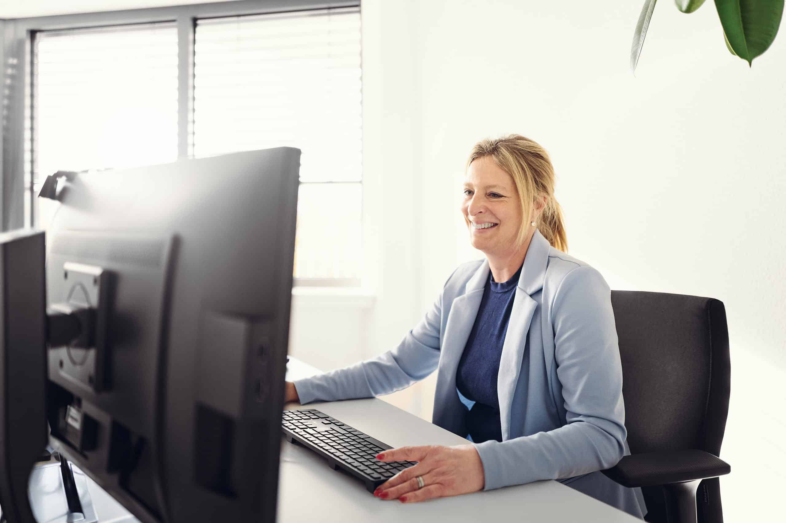 Christel Heusler sits smiling in front of her computer and works.
