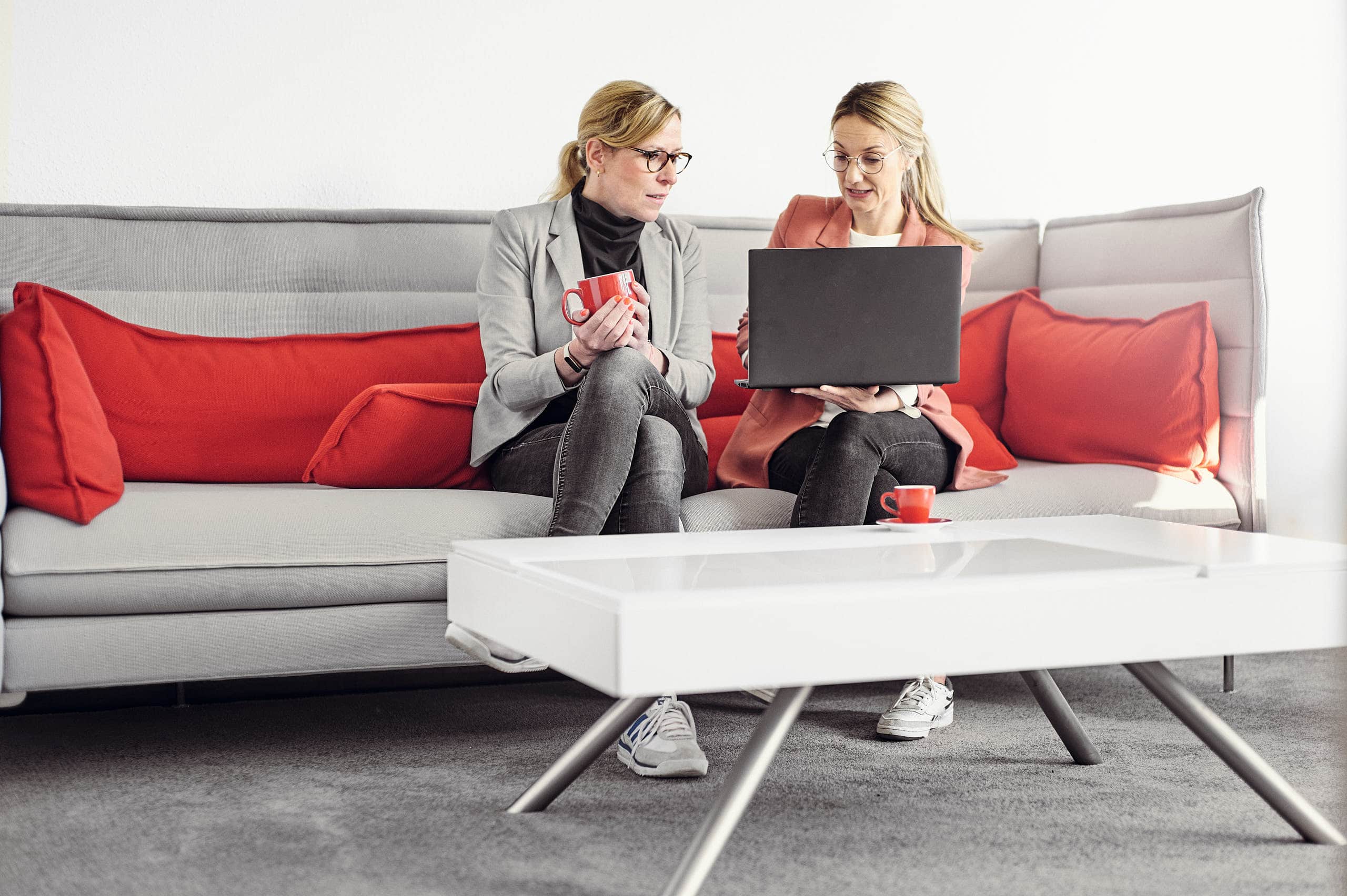 Celine Spitz and Magdalena Sabaß are sitting on a couch while Celine explains something to Magdalena on her laptop.