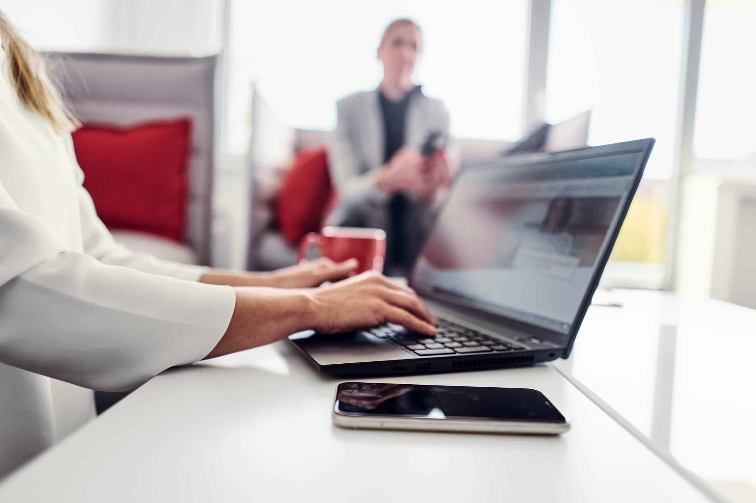 A person is sitting on the sofa in the kwsoft lounge and visiting the Kwsoft website on their laptop.