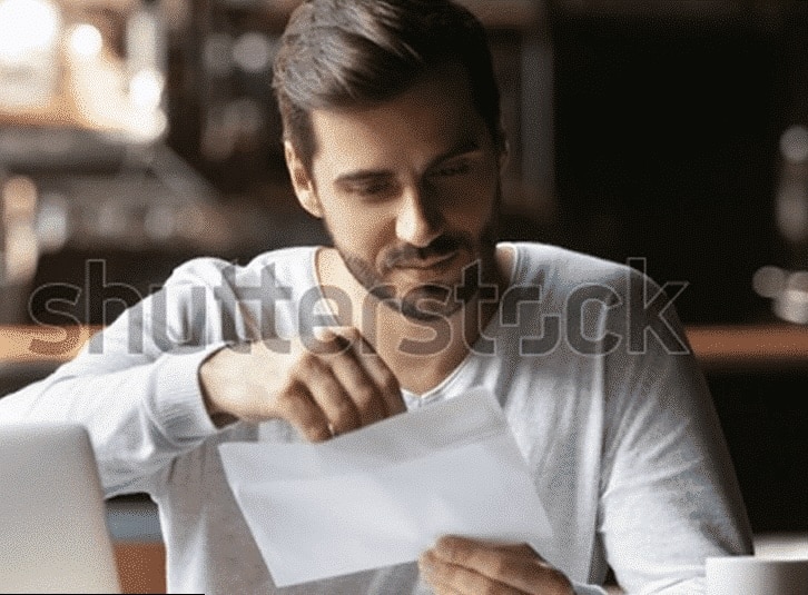 A man sits in a place and opens a letter.