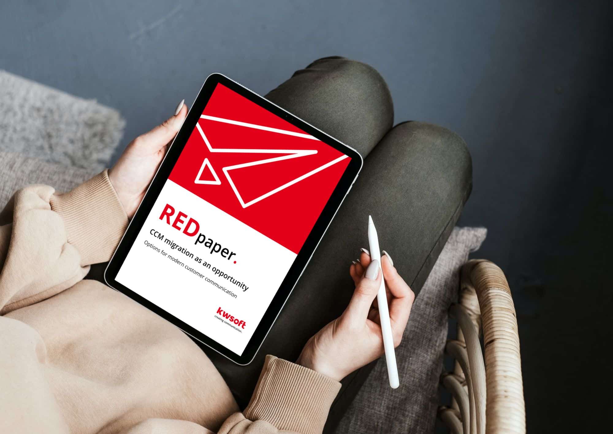 The image shows a tablet hold by someone which shows the cover of the REDpaper "CCM – Migration"